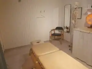 Behandlingsrum med massagebänk och medicinsk modell av skelett.