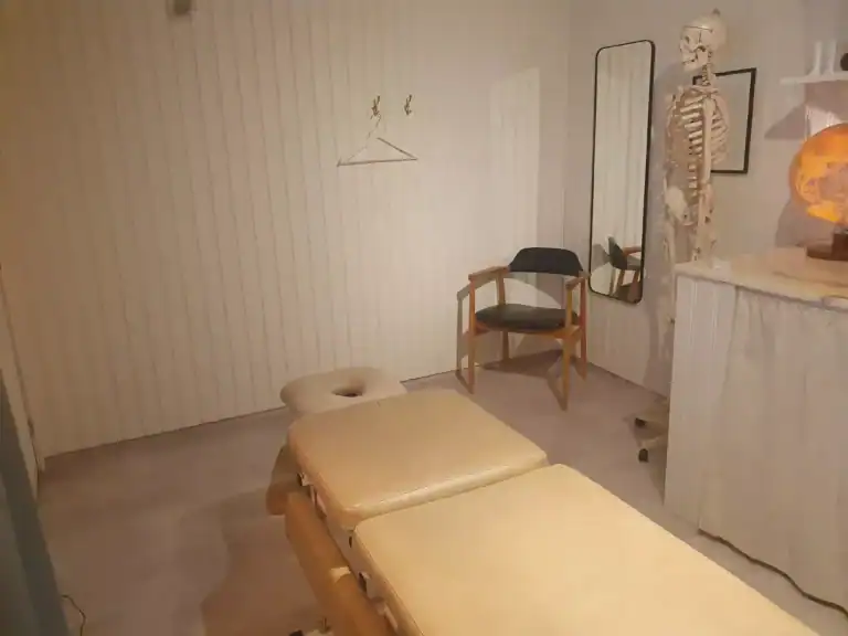 Behandlingsrum med massagebänk och medicinsk modell av skelett.