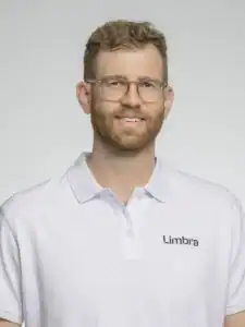 Man i vit Limbra-uniform med glasögon och skägg, ler mot kameran.