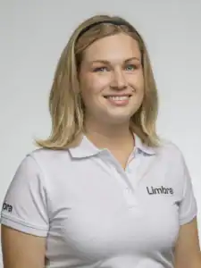 Kvinna i vit Limbra-uniform med leende och blont hår.
